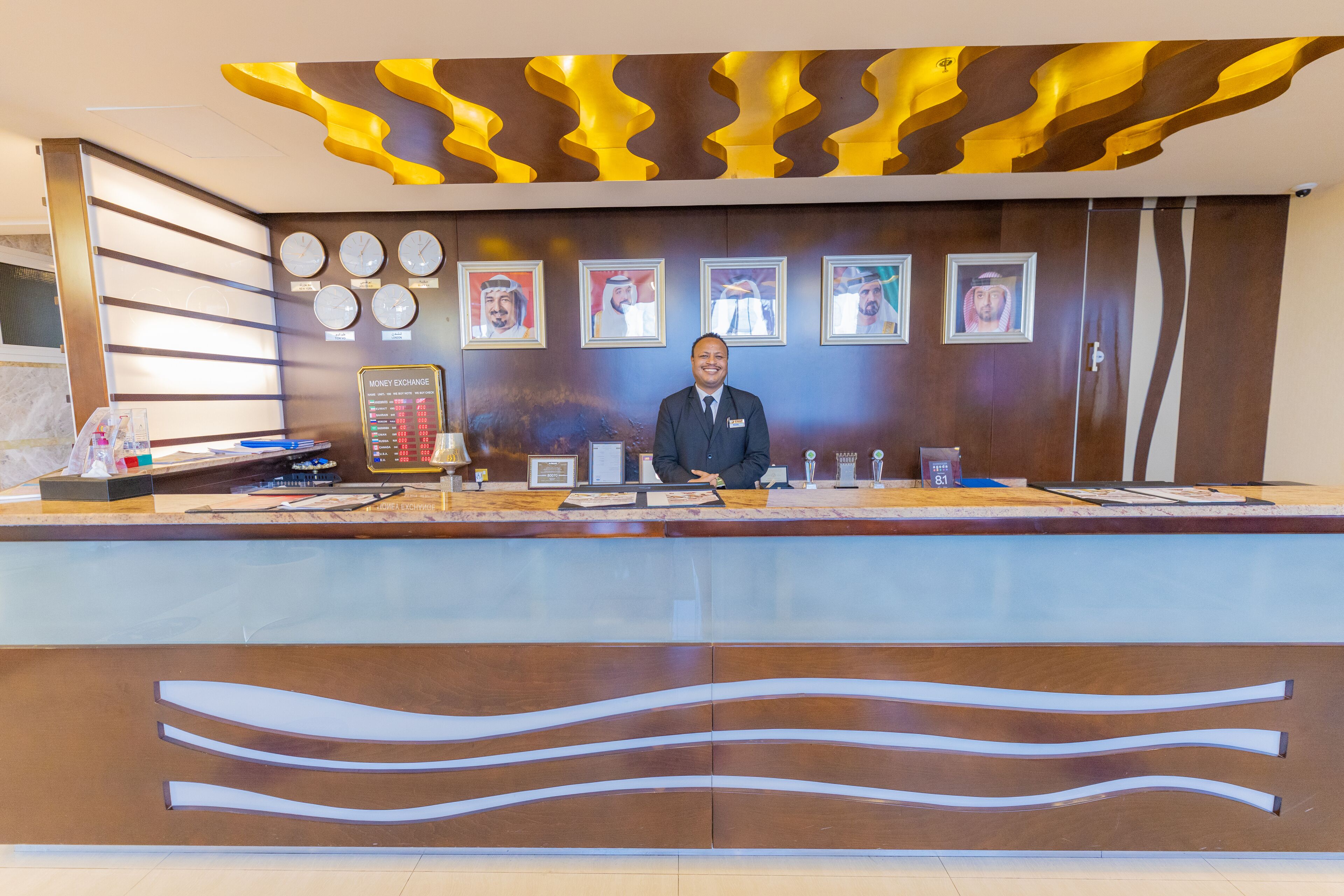 Een modern ontworpen receptiebalie, met een naamplaatje, een klok en ingekaderde foto's aan de muur.