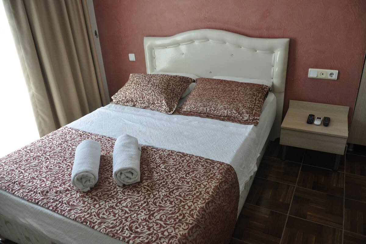 Una cama bien hecha con ropa de cama estampada, un cabecero blanco y una mesita de noche con un control remoto.