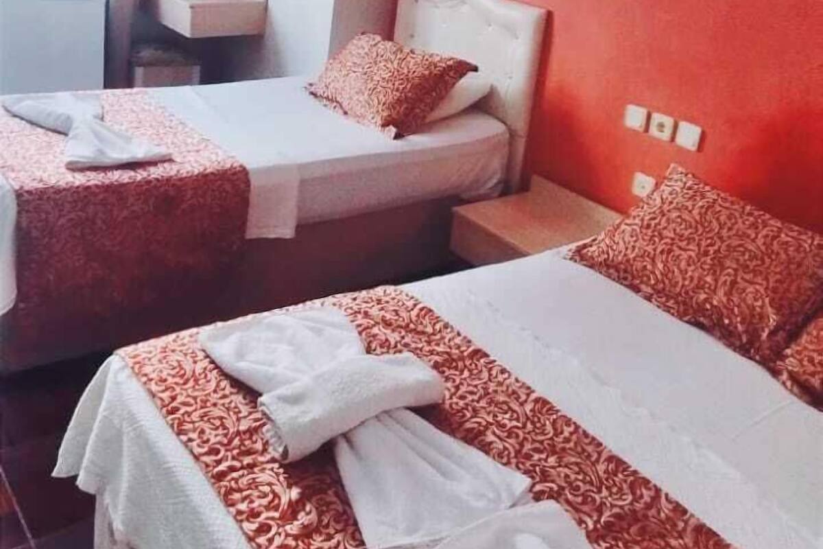Habitación de hotel con dos camas, una pared de acento roja, un equipo de aire acondicionado blanco y una ventana con cortinas.
