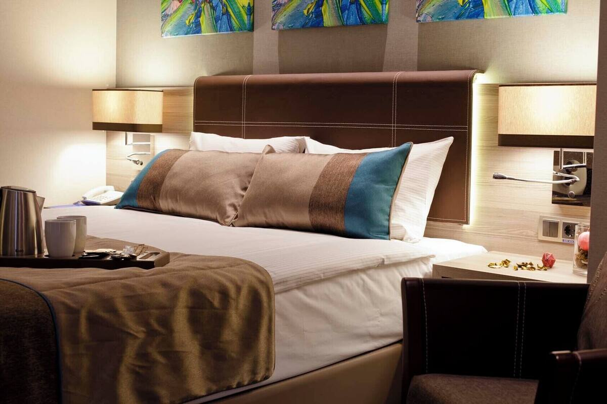 A hotel room with a large bed, bedside lamps, a coffee maker, and a small table with a cup and a decorative item.