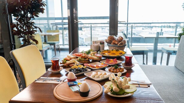 Una mesa de comedor con diversos platos, una taza de té y vistas a la ciudad a través de amplios ventanales.