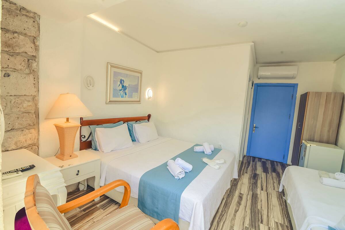 A hotel room with a bed, bedside table, lamp, and a blue door.