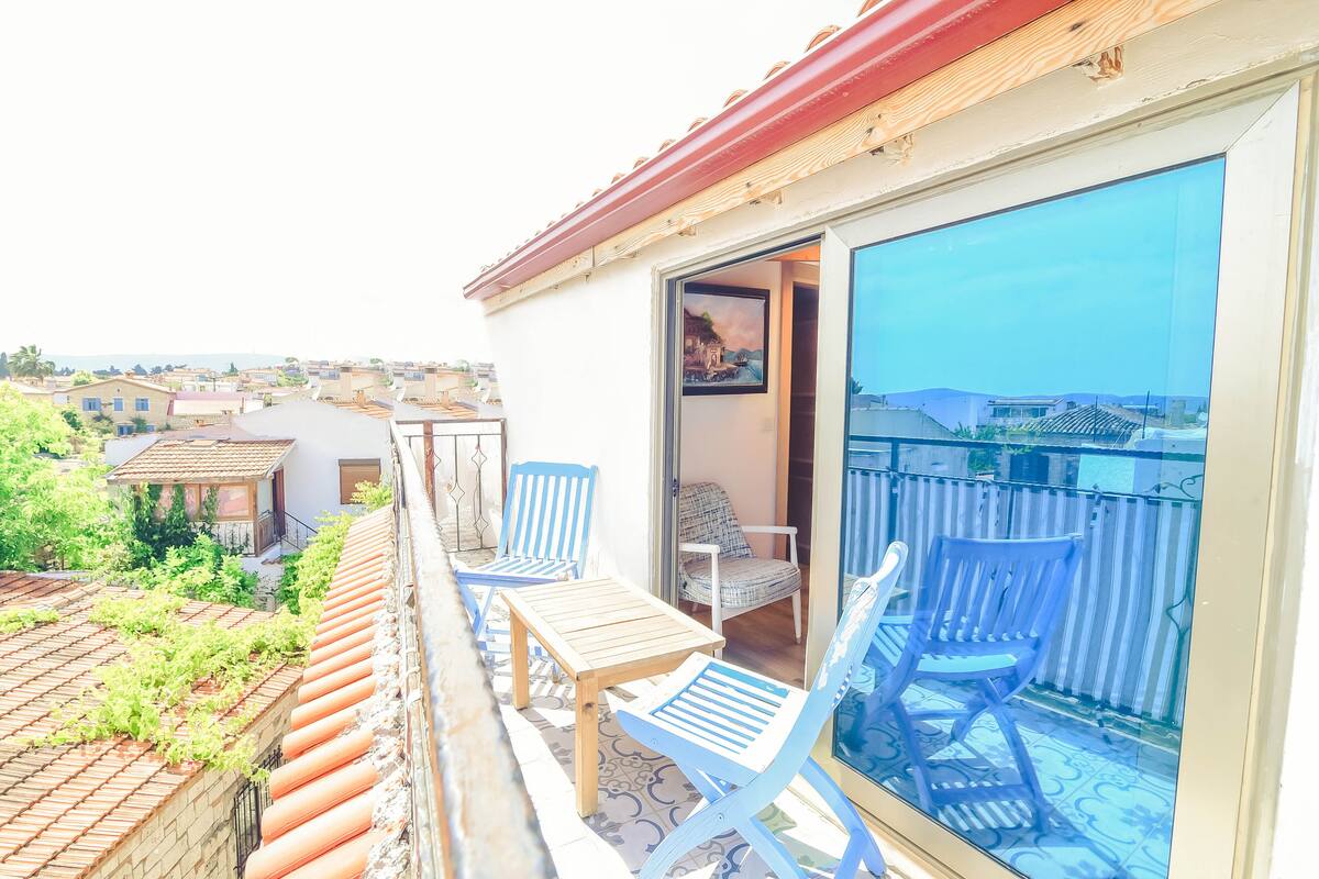 A balcony with blue chairs and a wooden table, overlooking a residential area.