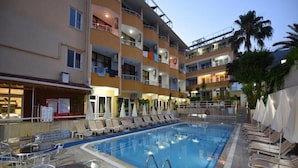 Una piscina con sillones y mesas, rodeada por un edificio de varios pisos con balcones.