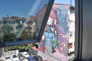 Finestra amb vista a un carrer i un mural colorit a l'edifici.