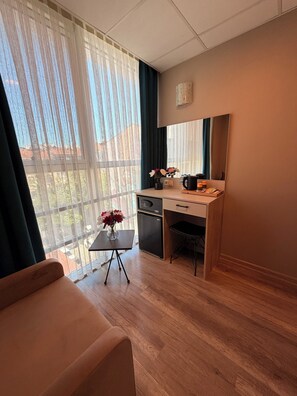 A compact room with a desk, a small refrigerator, a chair, a table with a vase of flowers, and a sofa. - Rota Hotel Kadıköy (Istanbul)