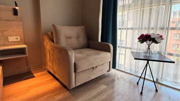Un salón moderno con un sofá beige, una mesita auxiliar con un jarrón y un ventanal con cortinas traslúcidas.