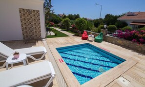 Una piscina con indicador de profundidad de 50 centímetros, rodeada por un solárium con baldosas, sillas de descanso blancas y plantas en macetas.