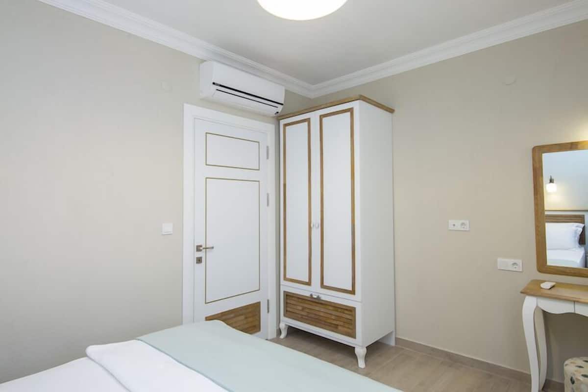 A bedroom with a bed, a wardrobe, an air conditioning unit, a mirror, and a bedside table.