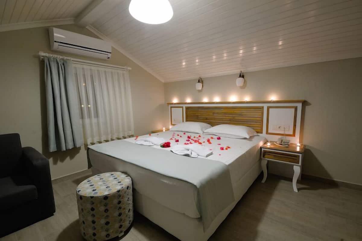 A hotel room with a bed, bedside table, lamp, air conditioning unit, and a small round table with a floral pattern.