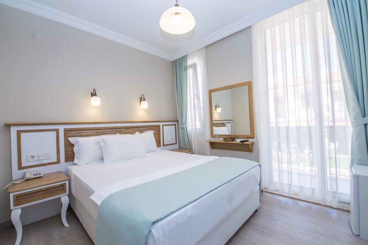 A hotel room with a large bed, bedside tables, a mirror, and a window with curtains.