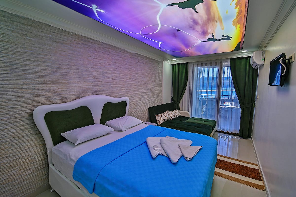 Une chambre d’hôtel avec un lit, une petite table, une chaise, une fresque au plafond et une fenêtre avec des rideaux.