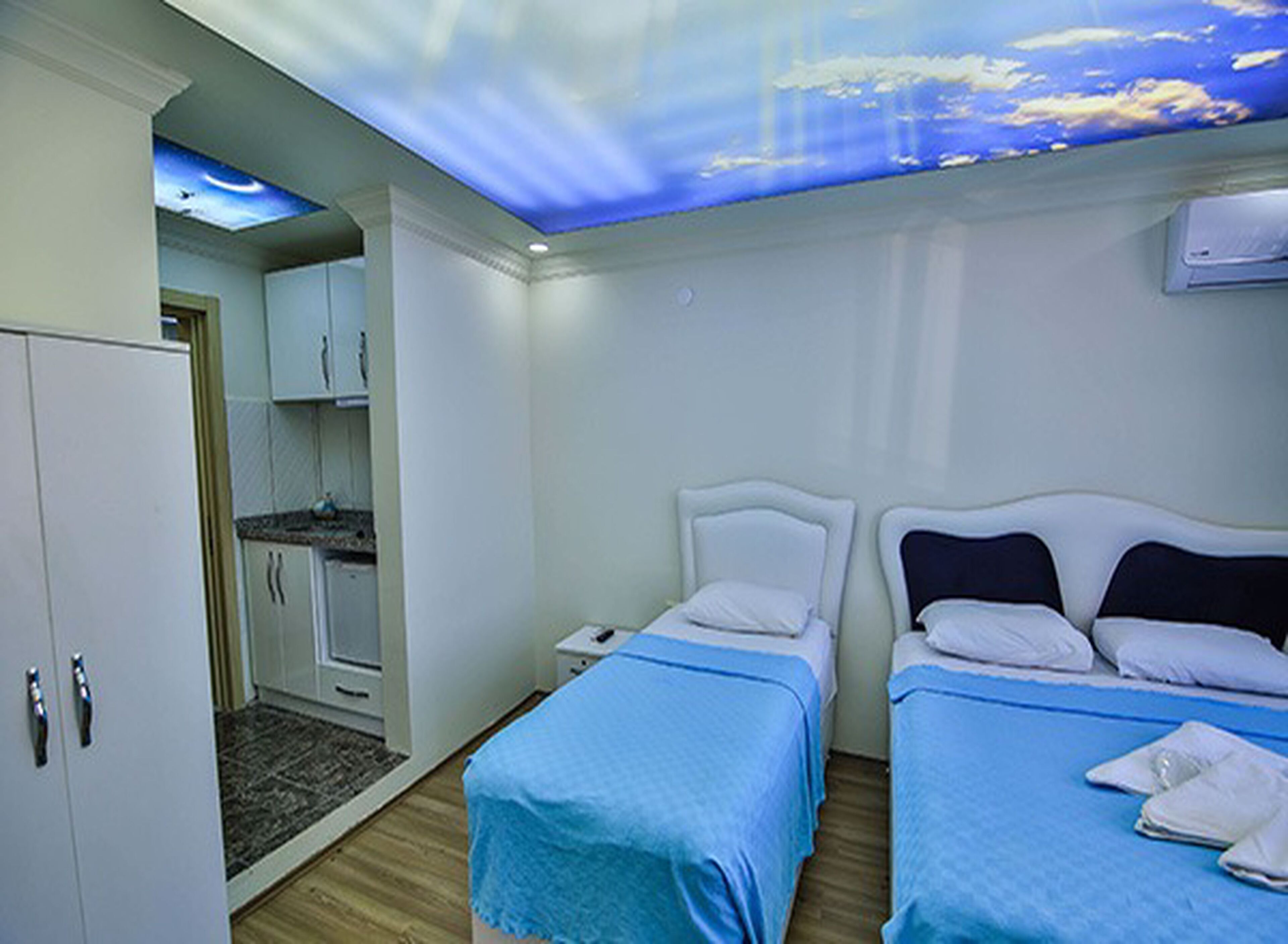 Habitación de hotel con dos camas, kitchenette y un techo decorado con un diseño de cielo y nubes.