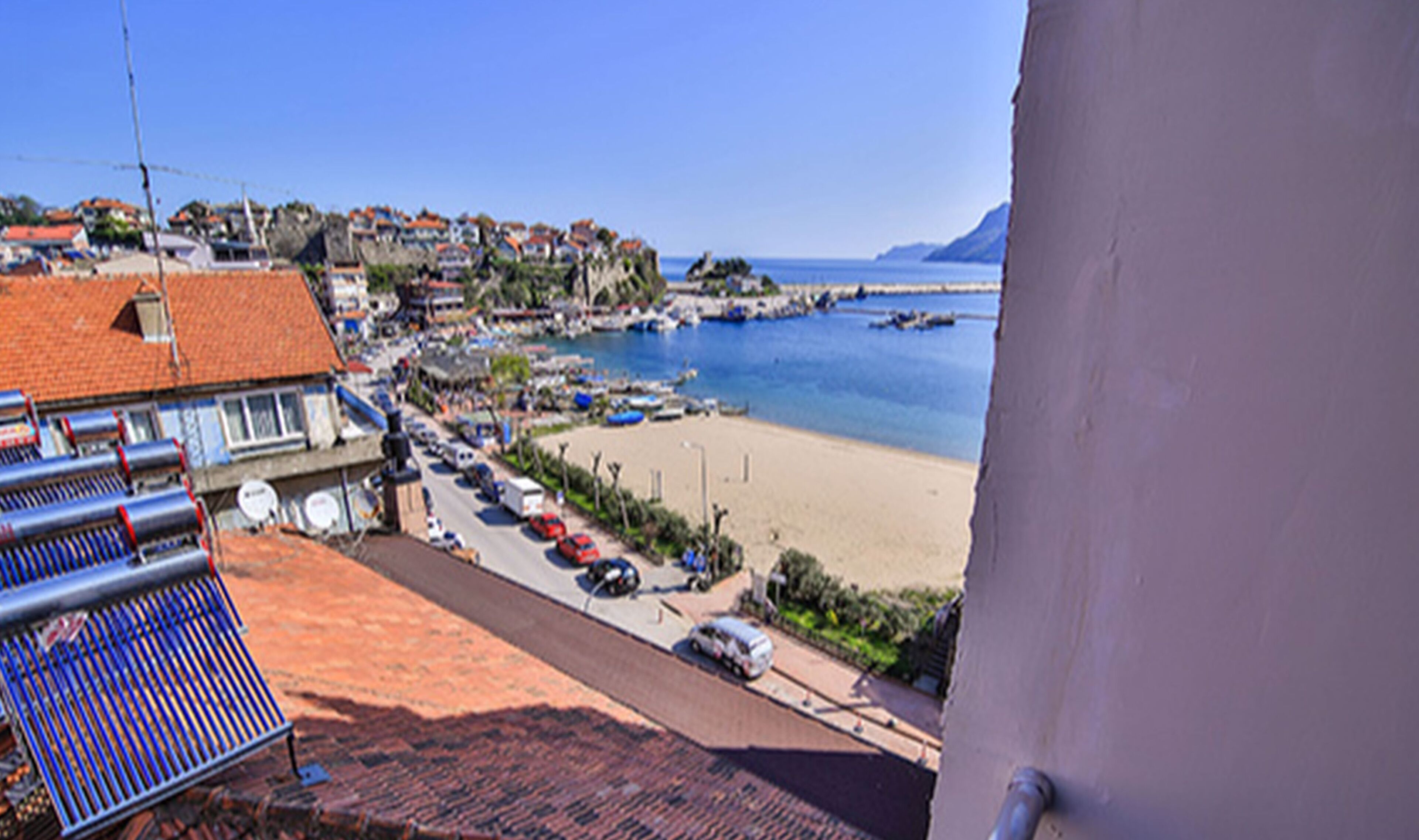 Un pueblo costero con playa, coches aparcados y edificios con tejados rojos.