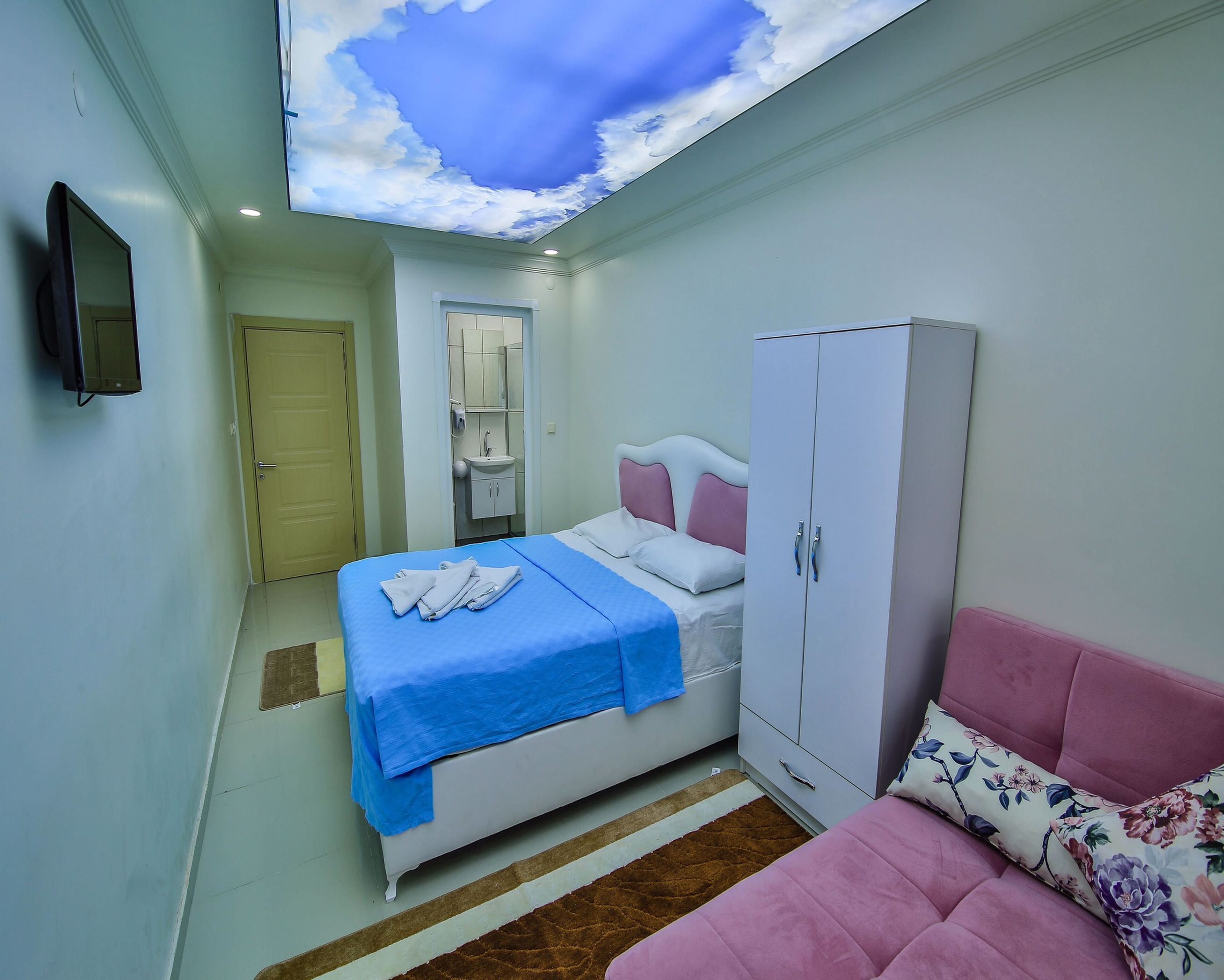 Quarto com cama, guarda-roupa e televisão na parede.
