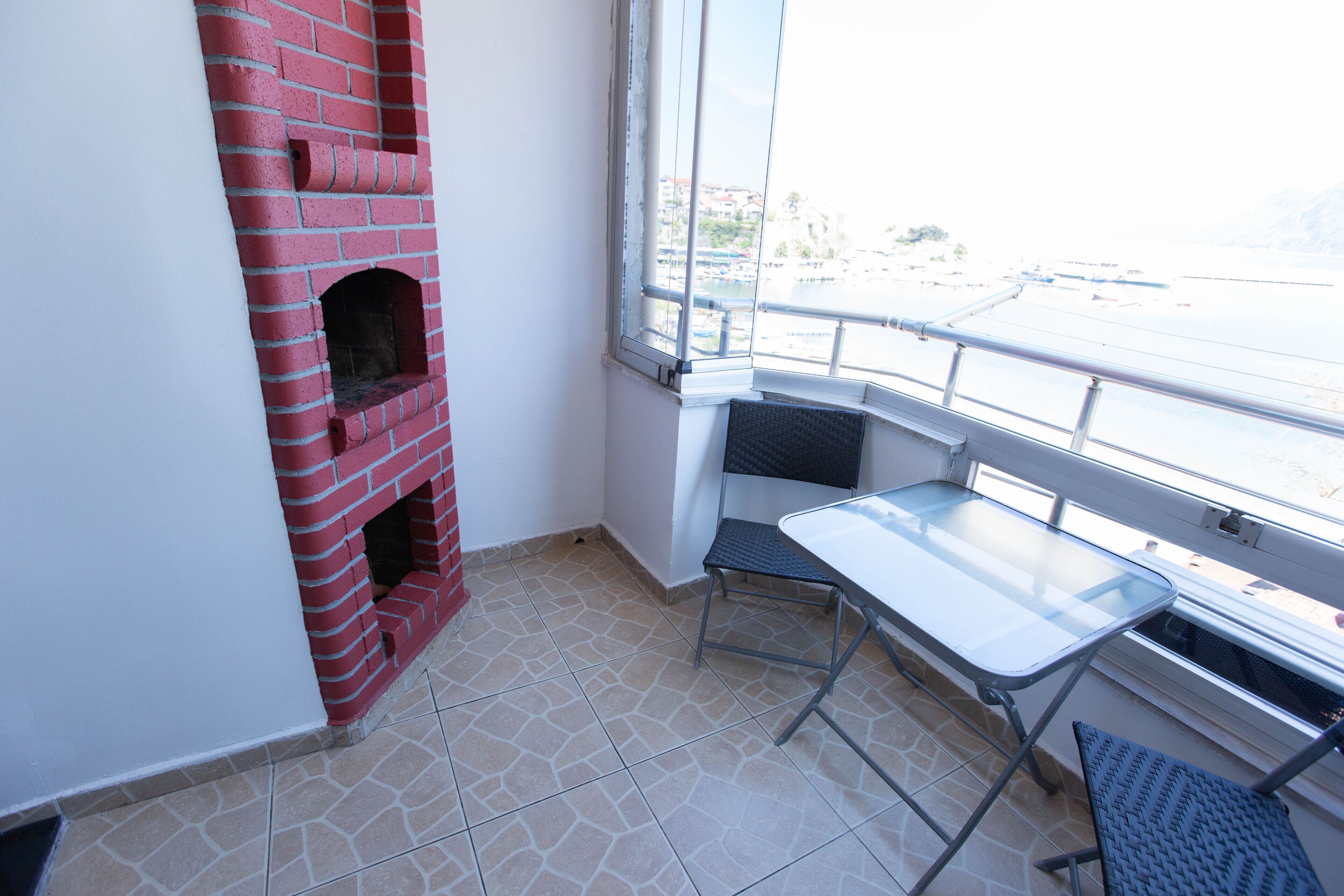 A small balcony with a red brick fireplace, a metal table, and a chair.