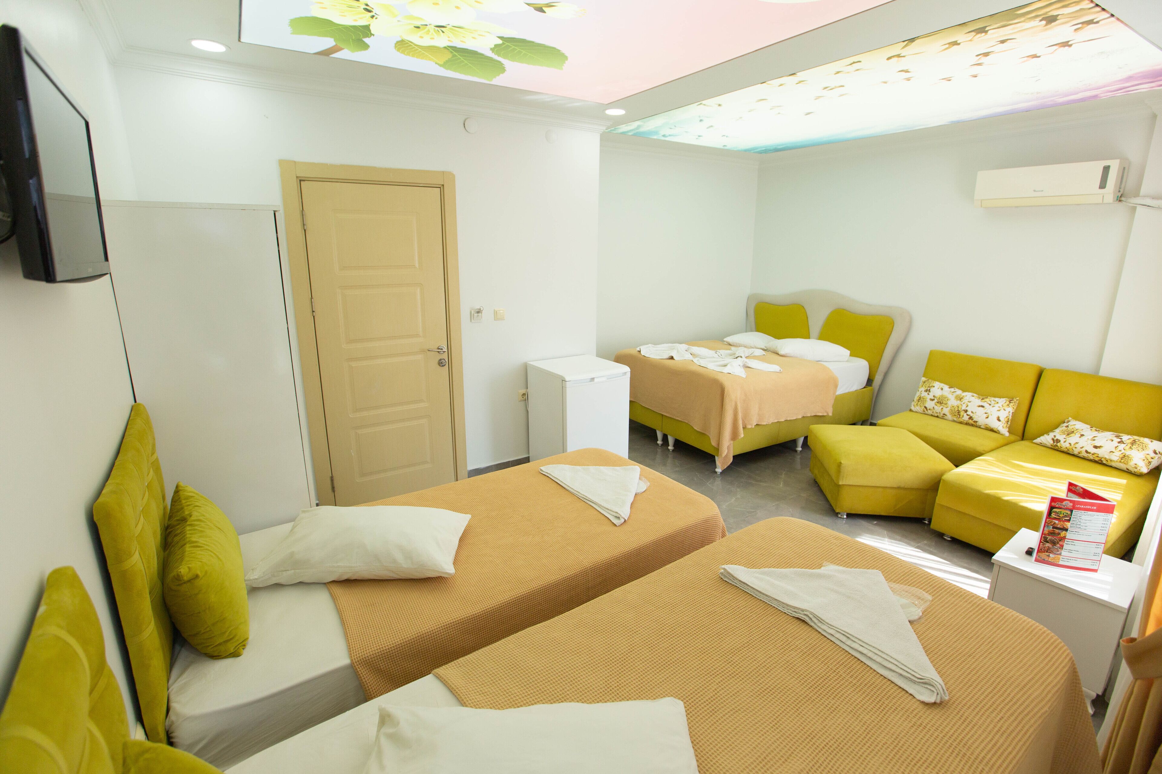 A hotel room with two beds, a small table, a sofa, a television, and an air conditioning unit.