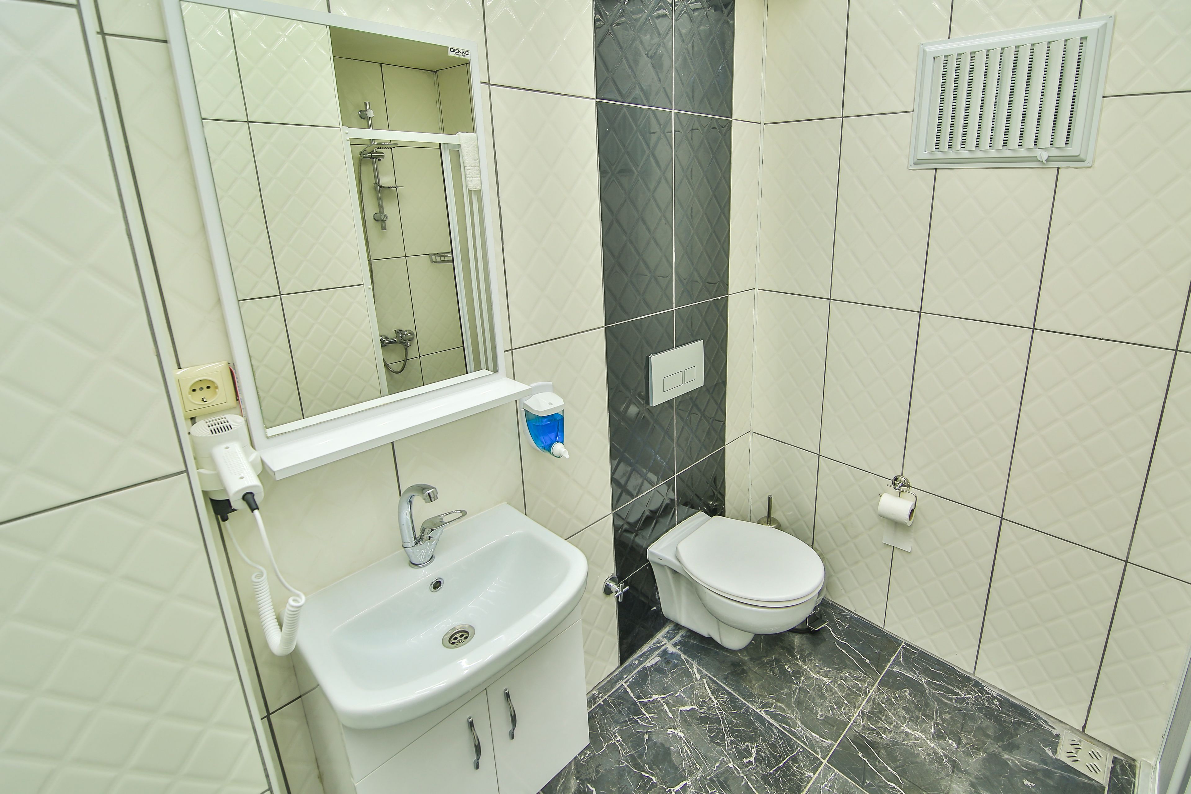 A bathroom with a white sink, a toilet, a mirror, and a shower area.