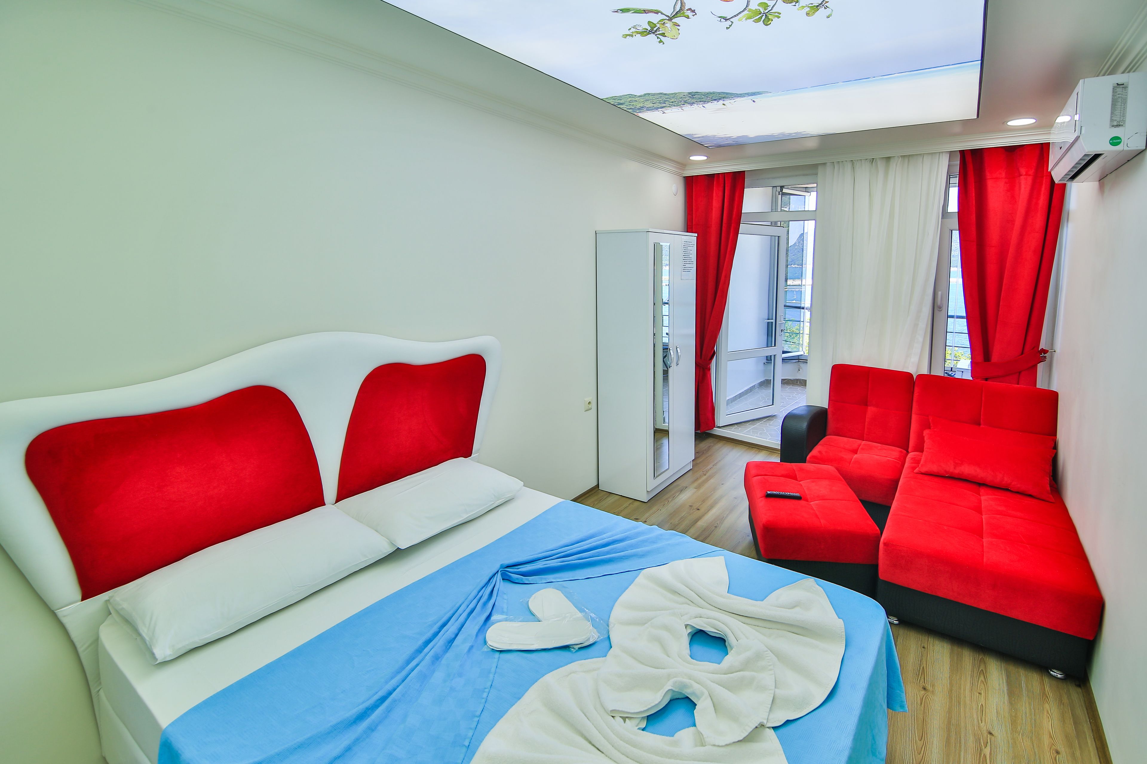 Una habitación de hotel con cama, sofá rojo, colcha azul y almohada blanca.