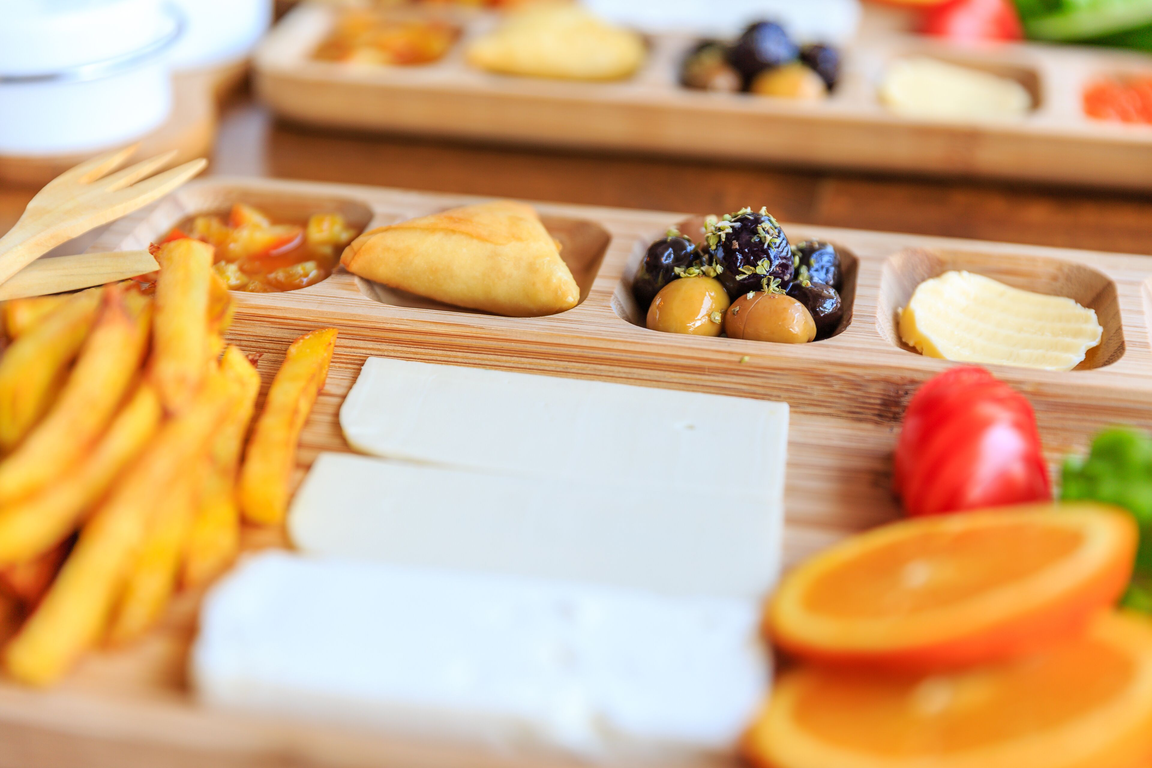 A wooden board with various food items including fries, a pastry, cheese, and sliced fruits.