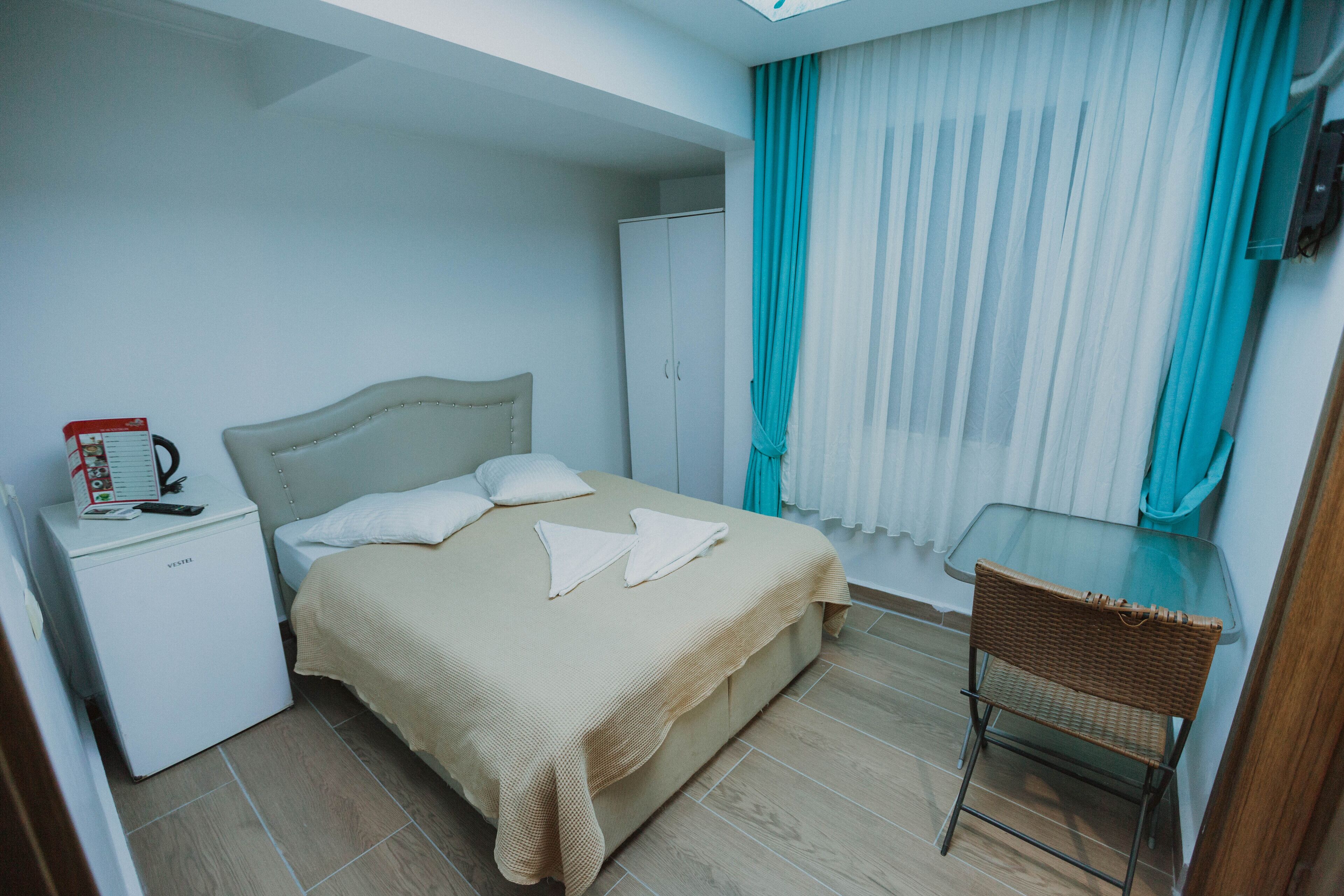 A hotel room with a bed, a small table, a chair, a wardrobe, and a window with curtains.