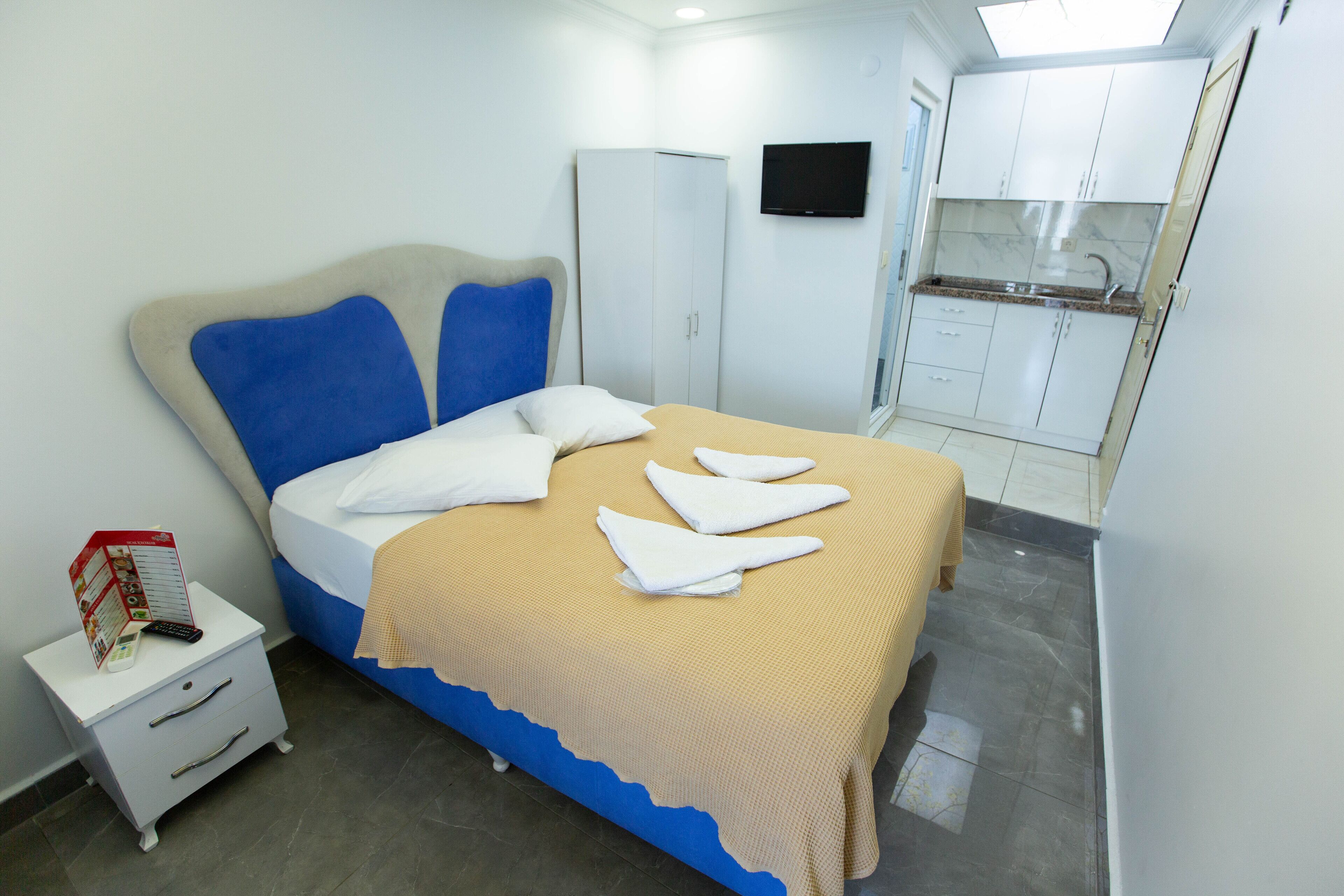A bedroom with a bed, a nightstand, a wardrobe, and a small kitchenette.