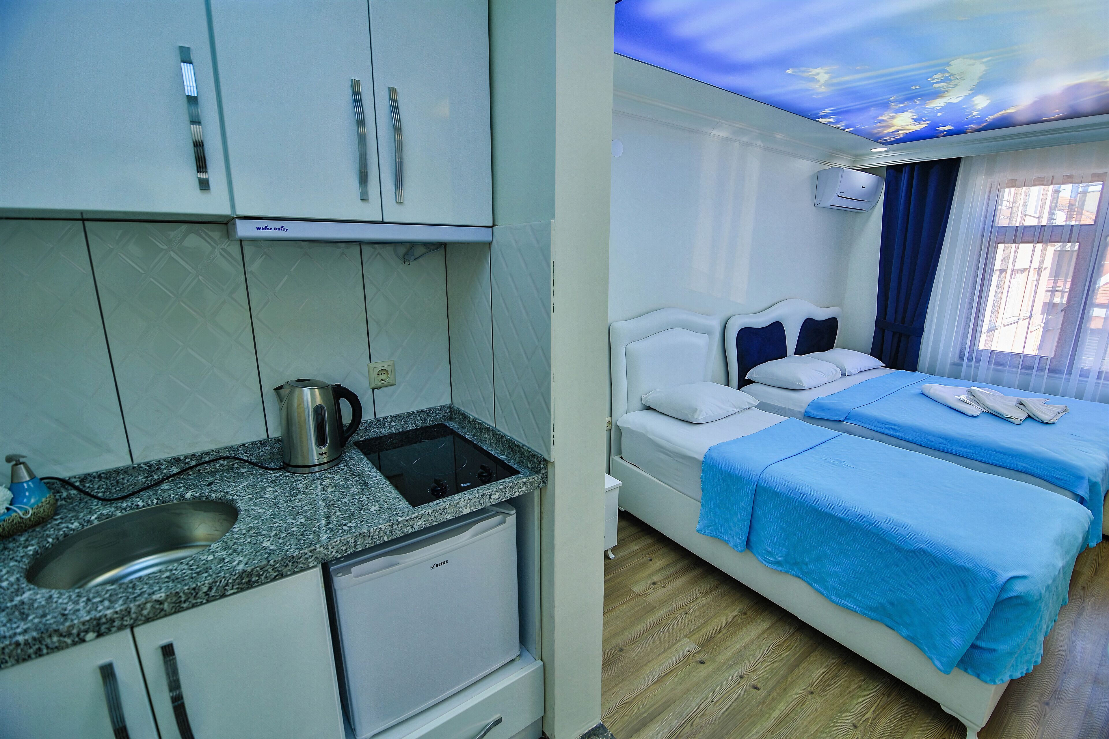 A compact hotel room with a kitchenette, a bed with blue bedding, and a ceiling with a starry sky design.