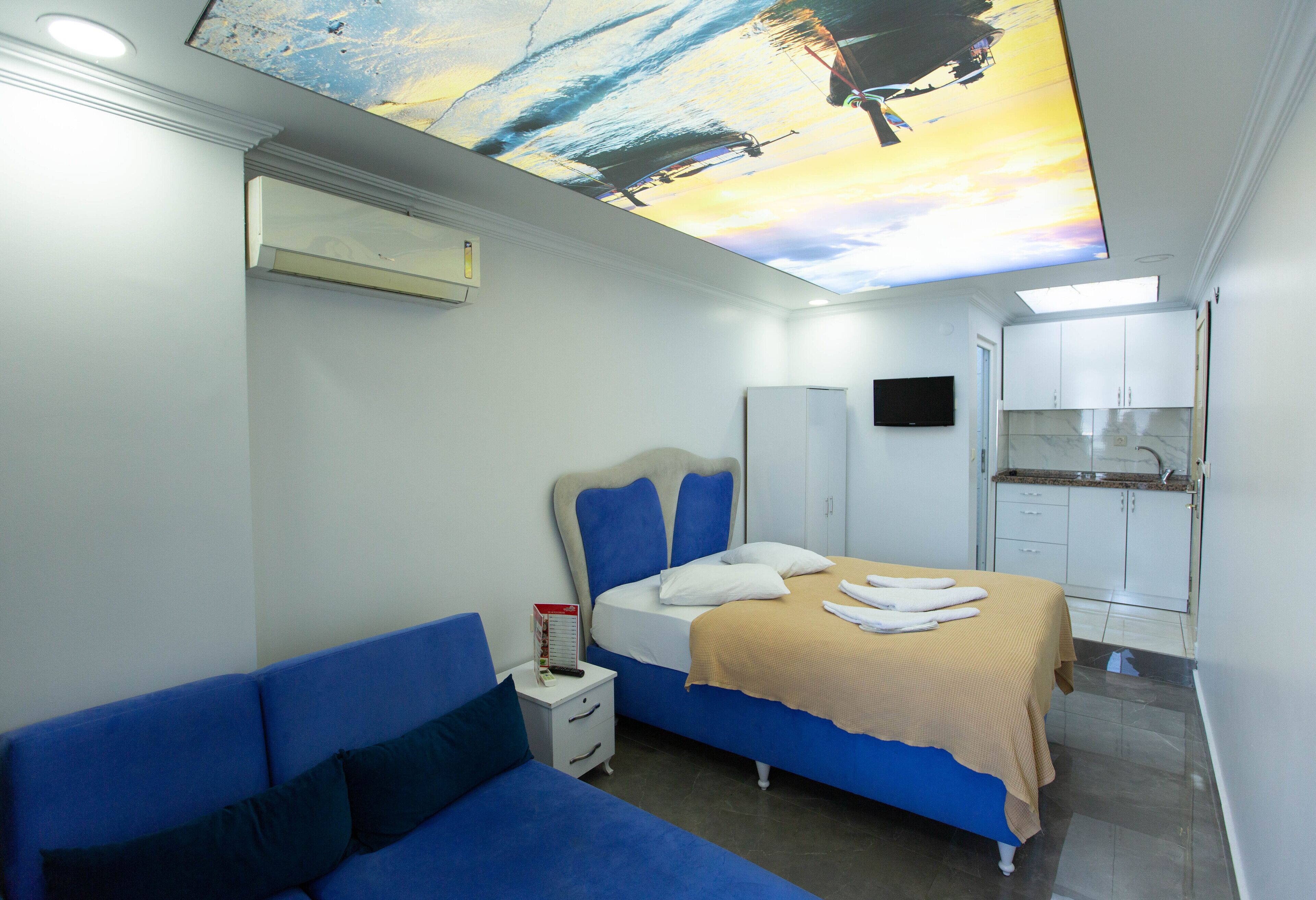 Une chambre d’hôtel moderne avec un lit, un canapé bleu, une petite table de chevet et une fresque au plafond.