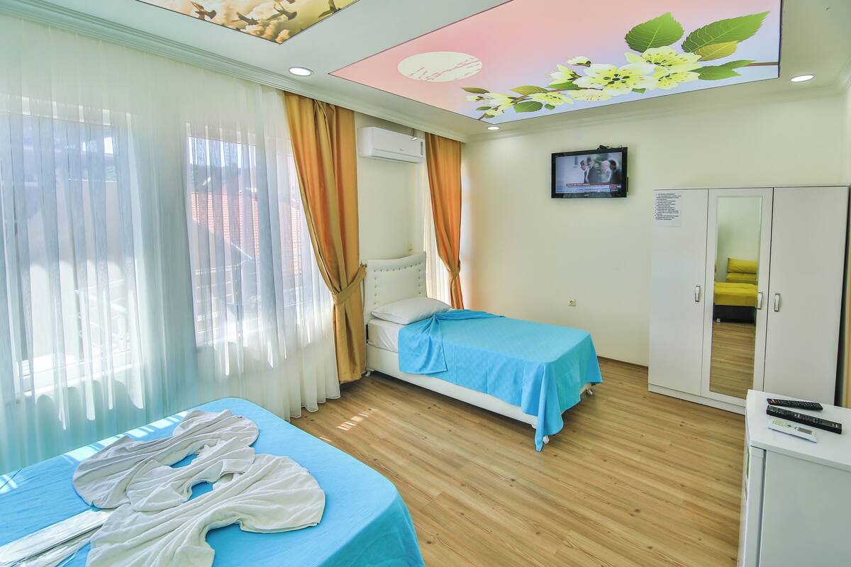 Une chambre d’hôtel avec deux lits, une armoire, un téléviseur et un plafond décoré de motifs floraux.