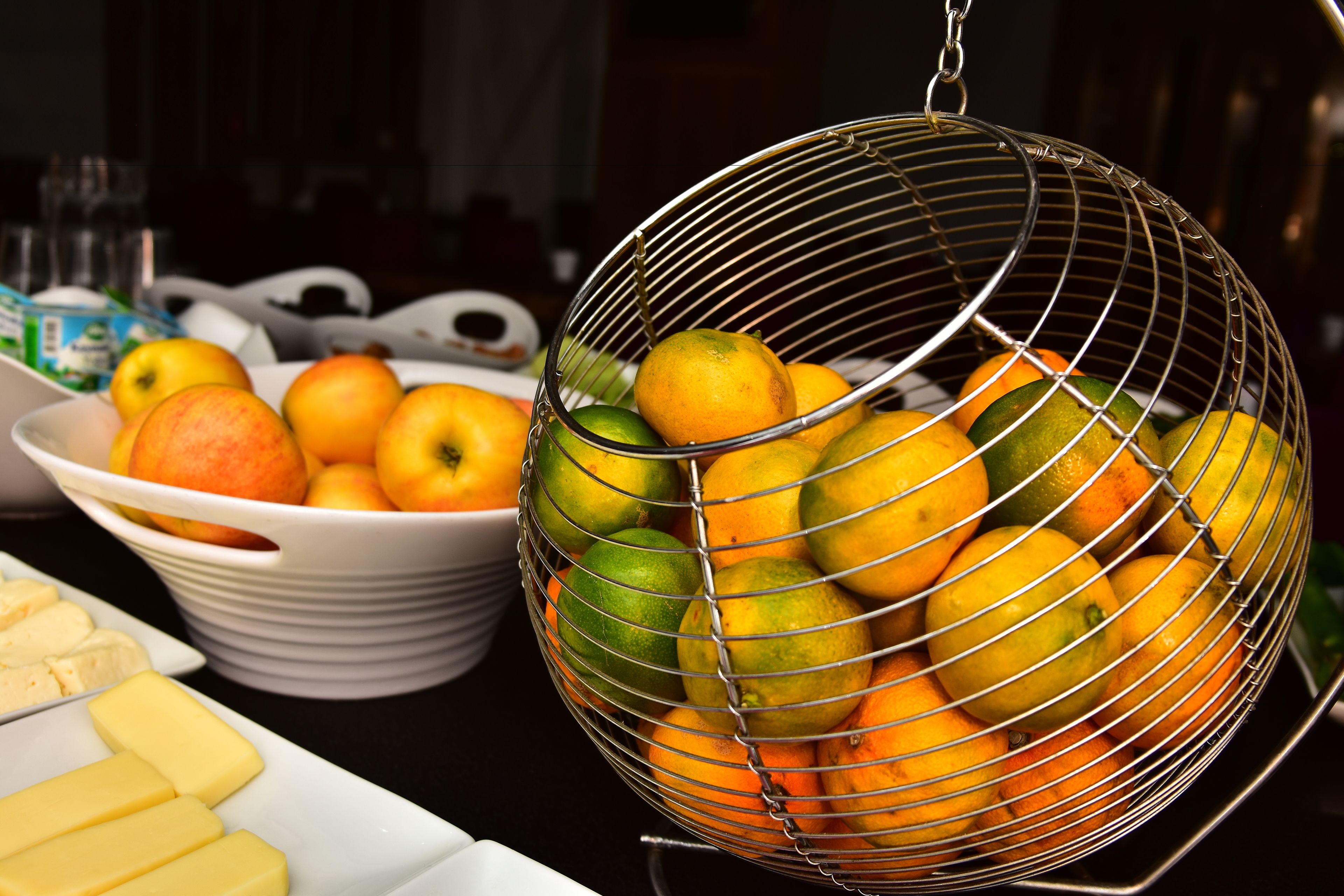 A fruit bowl with apples and oranges, and a hanging fruit basket with lemons and limes.