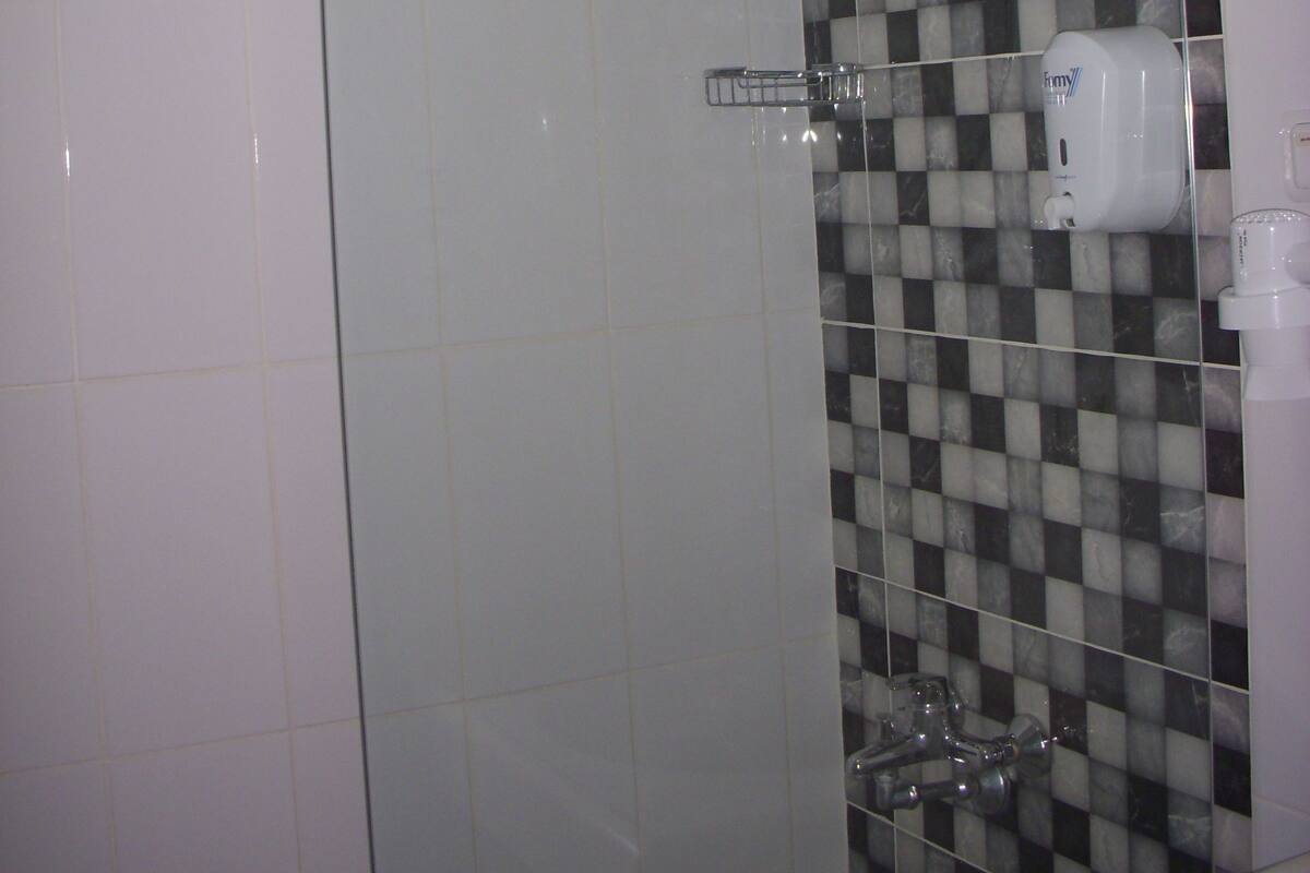 A shower with a glass door, a checkered tile wall, and a handheld showerhead.
