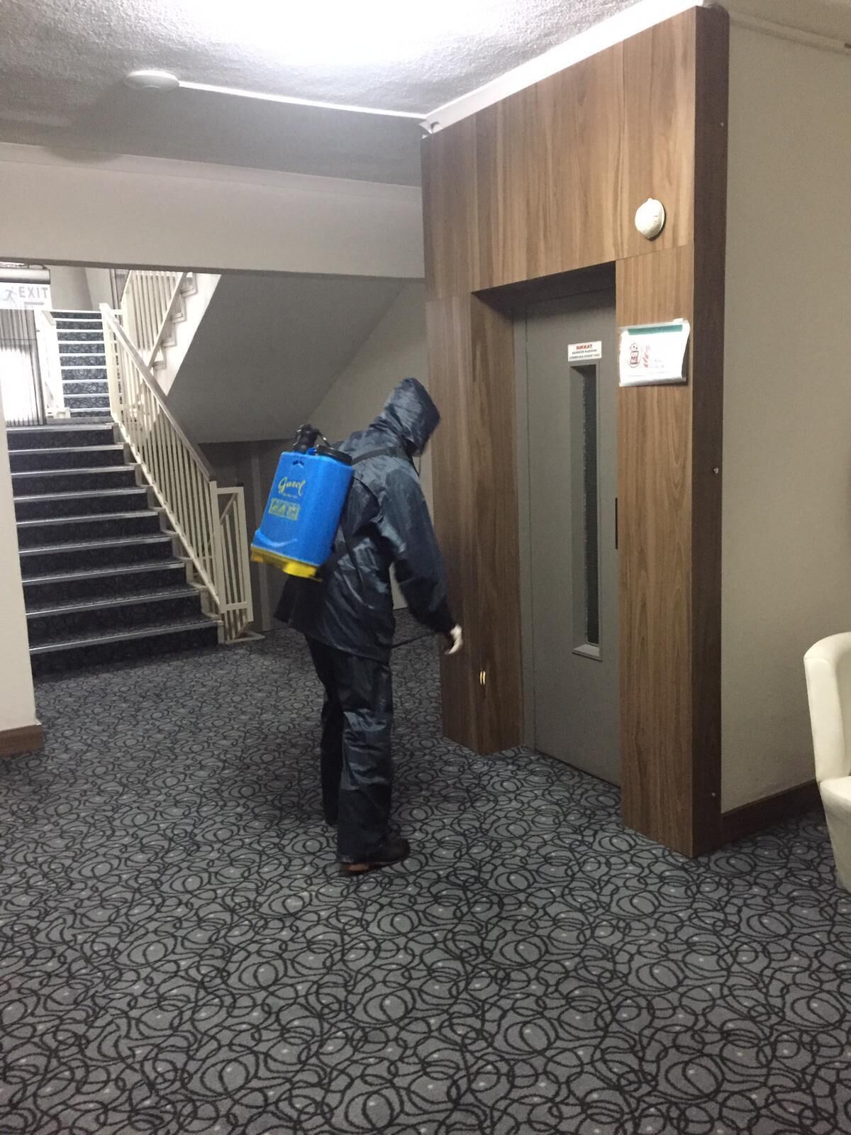 A person in a raincoat with a blue bag walking towards a door with a sign above it.