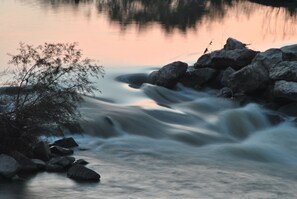 Ein Fluss fließt durch eine felsige Landschaft, links stehen Bäume.