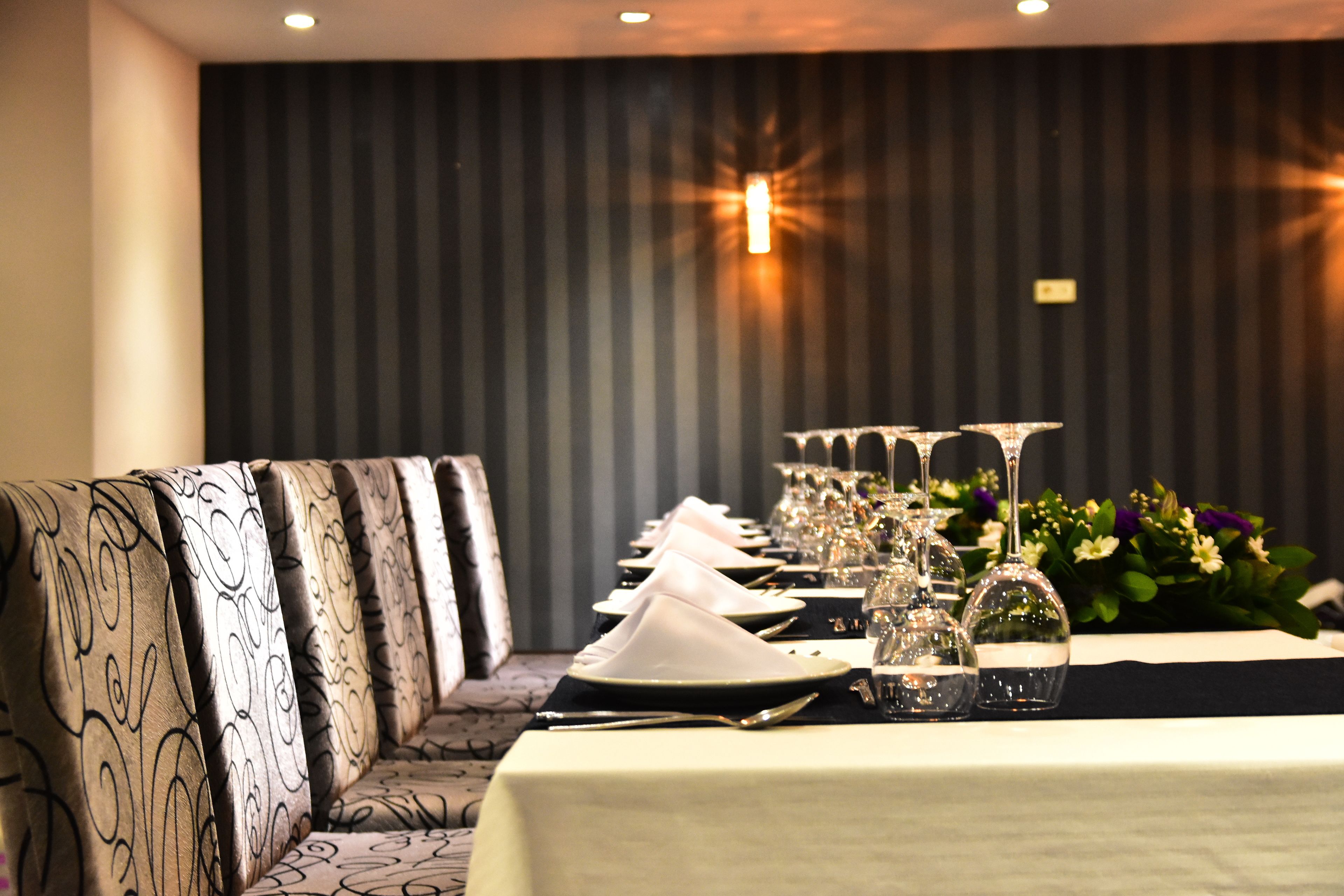 Una mesa de comedor con servilletas blancas, platos y cristalería, flanqueada por sillones estampados.
