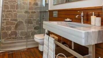 A bathroom with a stone wall, wooden floor, a large mirror, and a shower area.