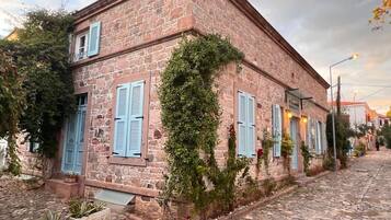 Un bâtiment en pierre avec des volets bleus, une rue pavée et un ciel dégagé.