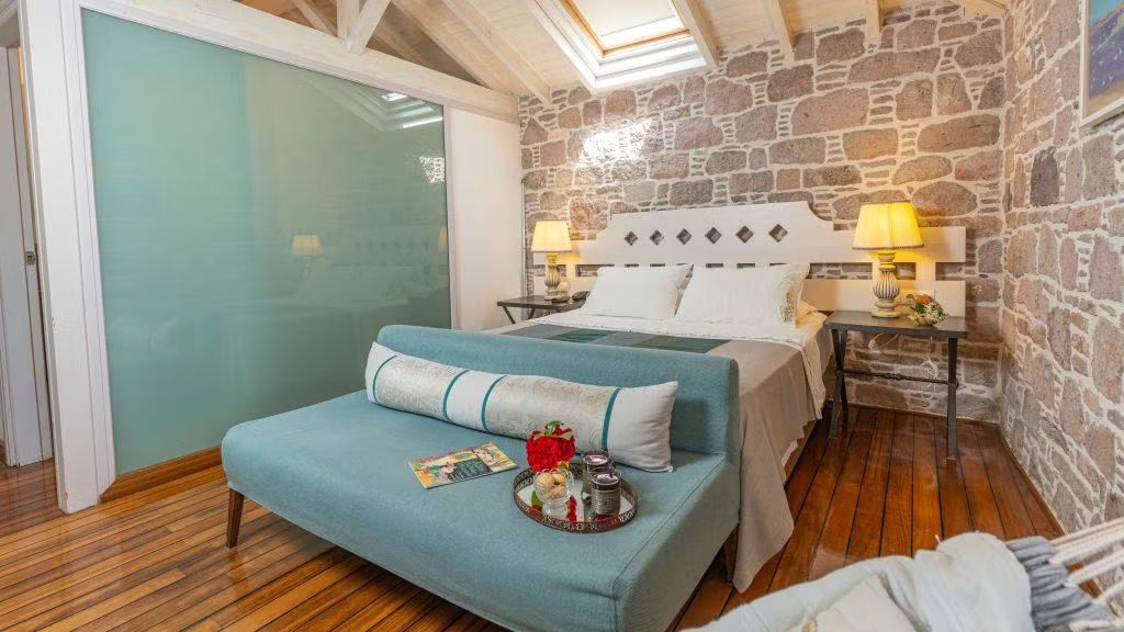 Un dormitorio con cama, un banco con bandeja y una pared de piedra.