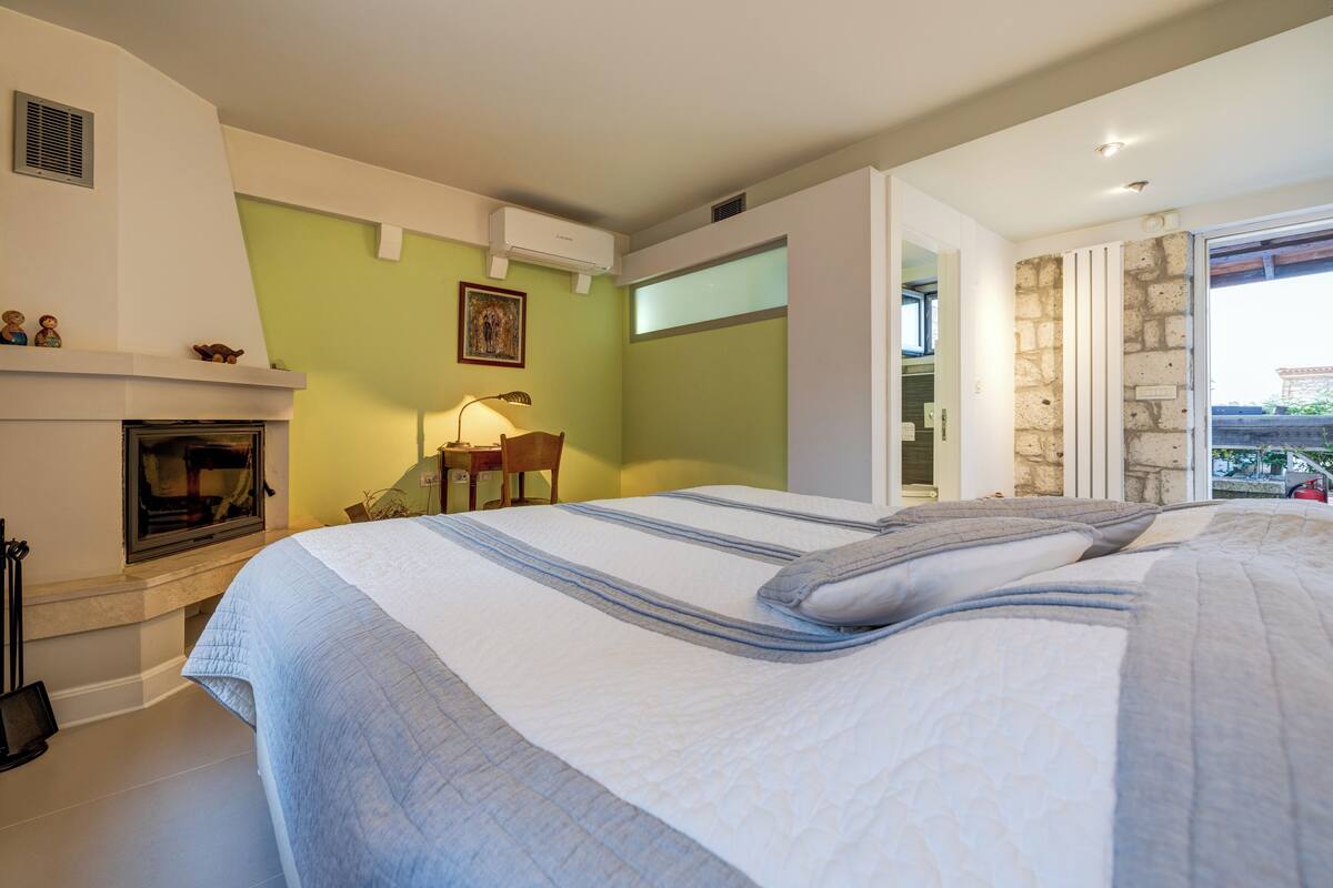 A bedroom with a large bed, a fireplace, a desk, and a view of the outside.