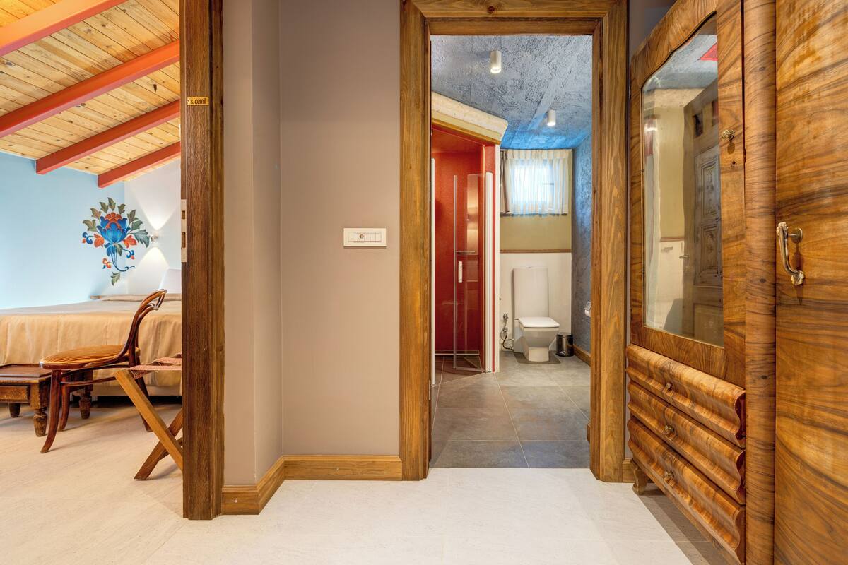 A room with a wooden ceiling, a bed, a chair, and a wooden cabinet.
