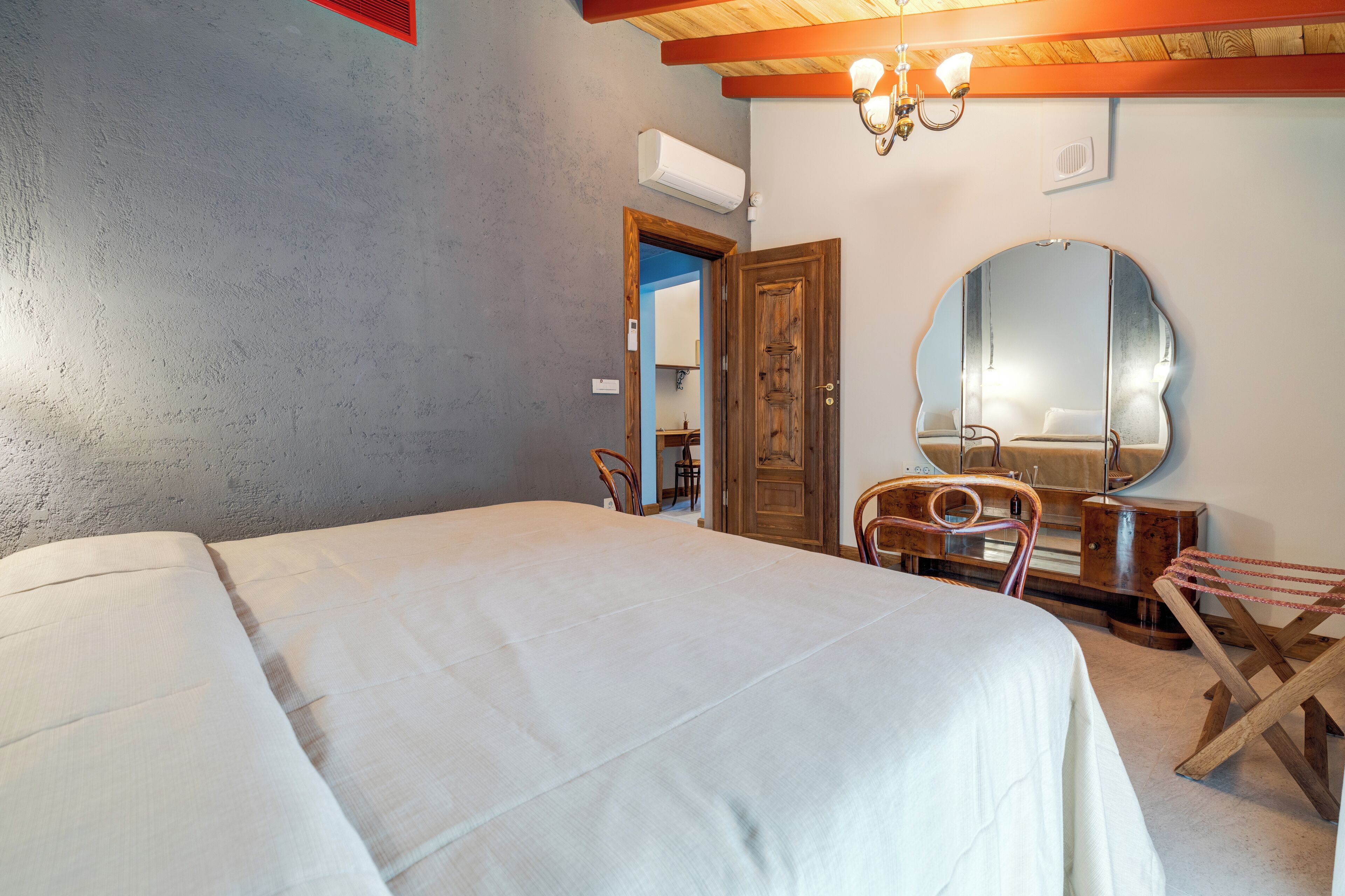 A bedroom with a large bed, a wooden dresser, a mirror, and a door leading to another room.