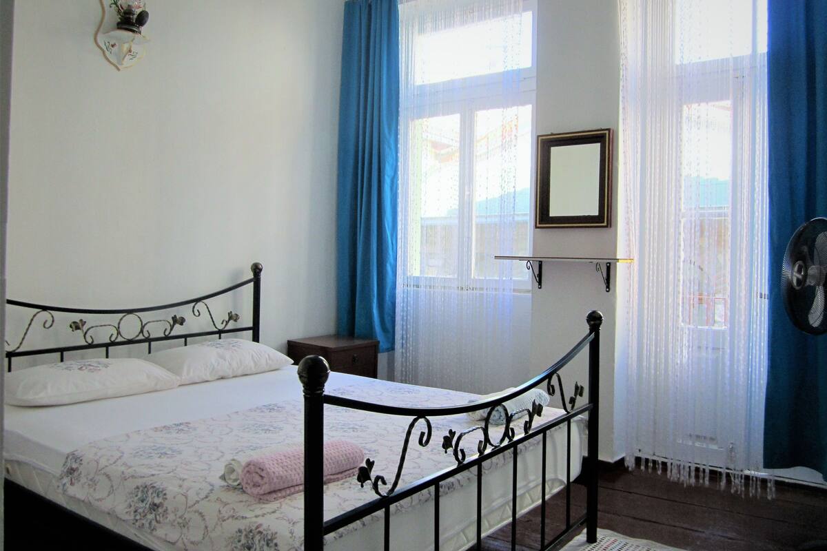A bedroom with a bed, a nightstand, a mirror, and a window with curtains.