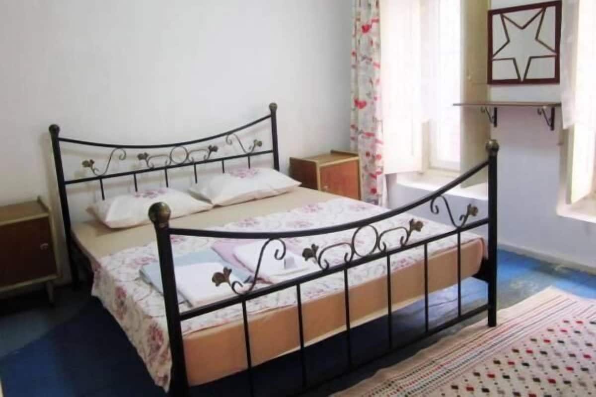 A single bed with a metal frame and floral bedding in a room with a blue carpet and a patterned rug.