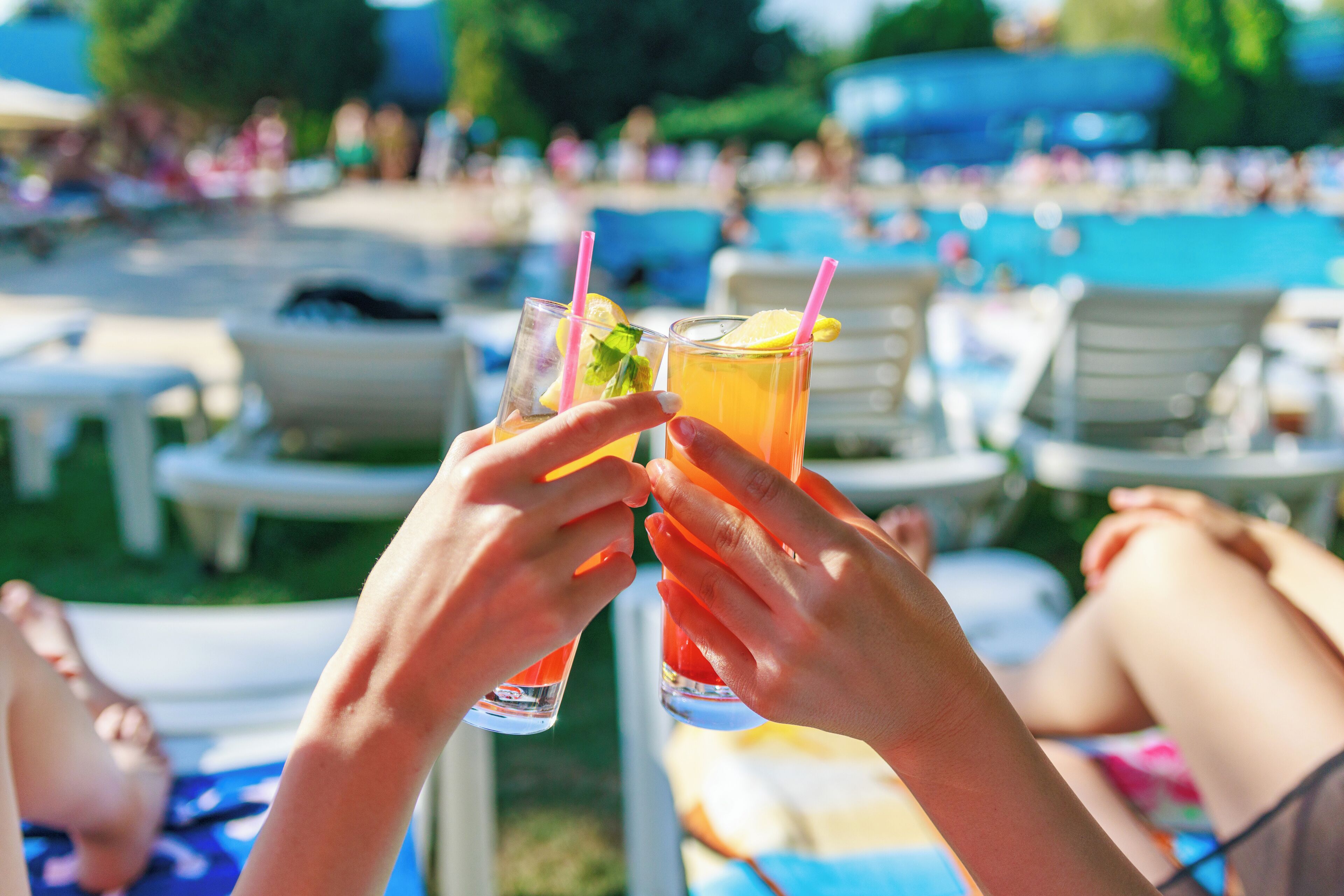 Due persone che sorseggiano un drink, con una piscina e lettini da relax sullo sfondo.