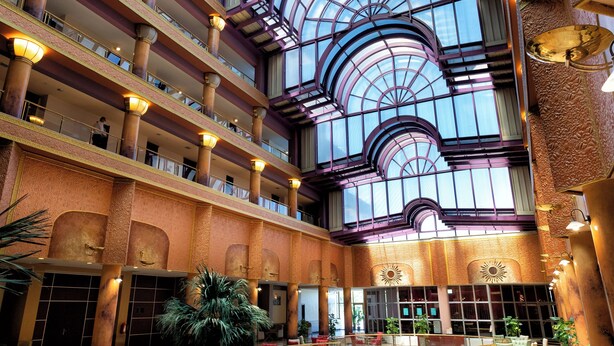 Een atrium met meerdere verdiepingen, een glazen dak en een centrale trap.