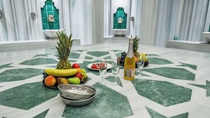 Een eettafel met fruit, een fles en glazen, geplaatst op een kamer met een patroon vloer, marmeren muren en groene accenten.