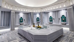 Een ruime kamer met een centraal marmeren plateau, een rond dakvenster en een decoratief groen embleem aan het plafond.