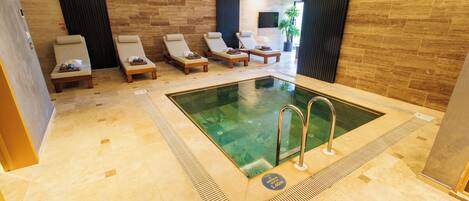 Un espace piscine intérieur moderne, doté de chaises longues et d’une eau cristalline.