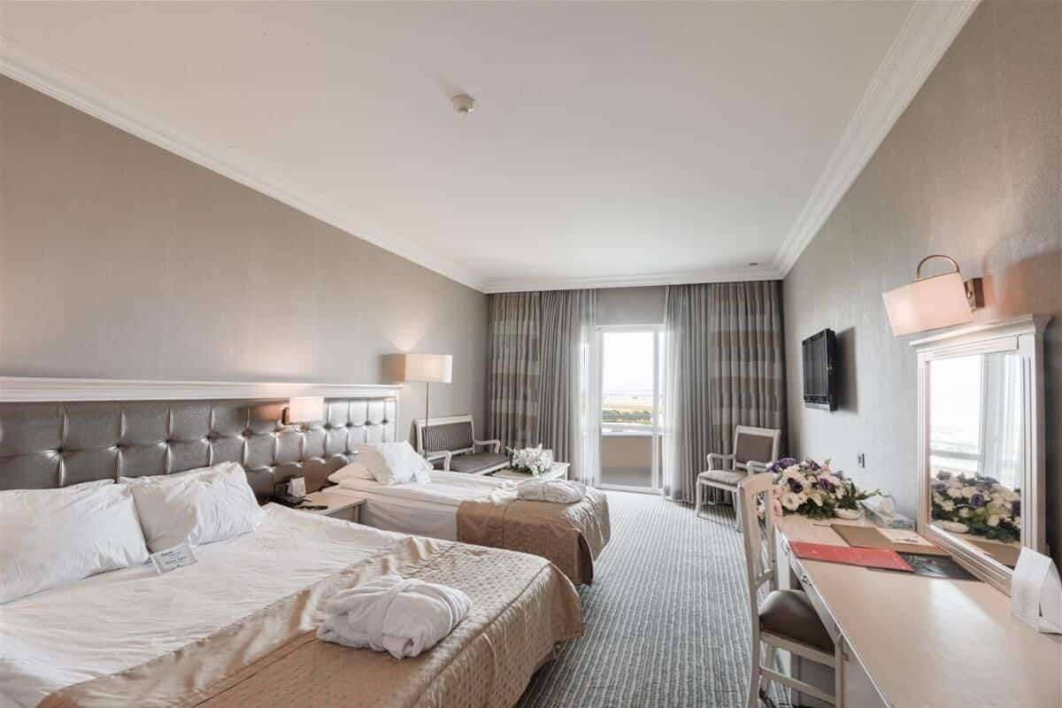 Ett hotellrum med två sängar, ett skrivbord, en stol, en TV och ett fönster med gardiner.