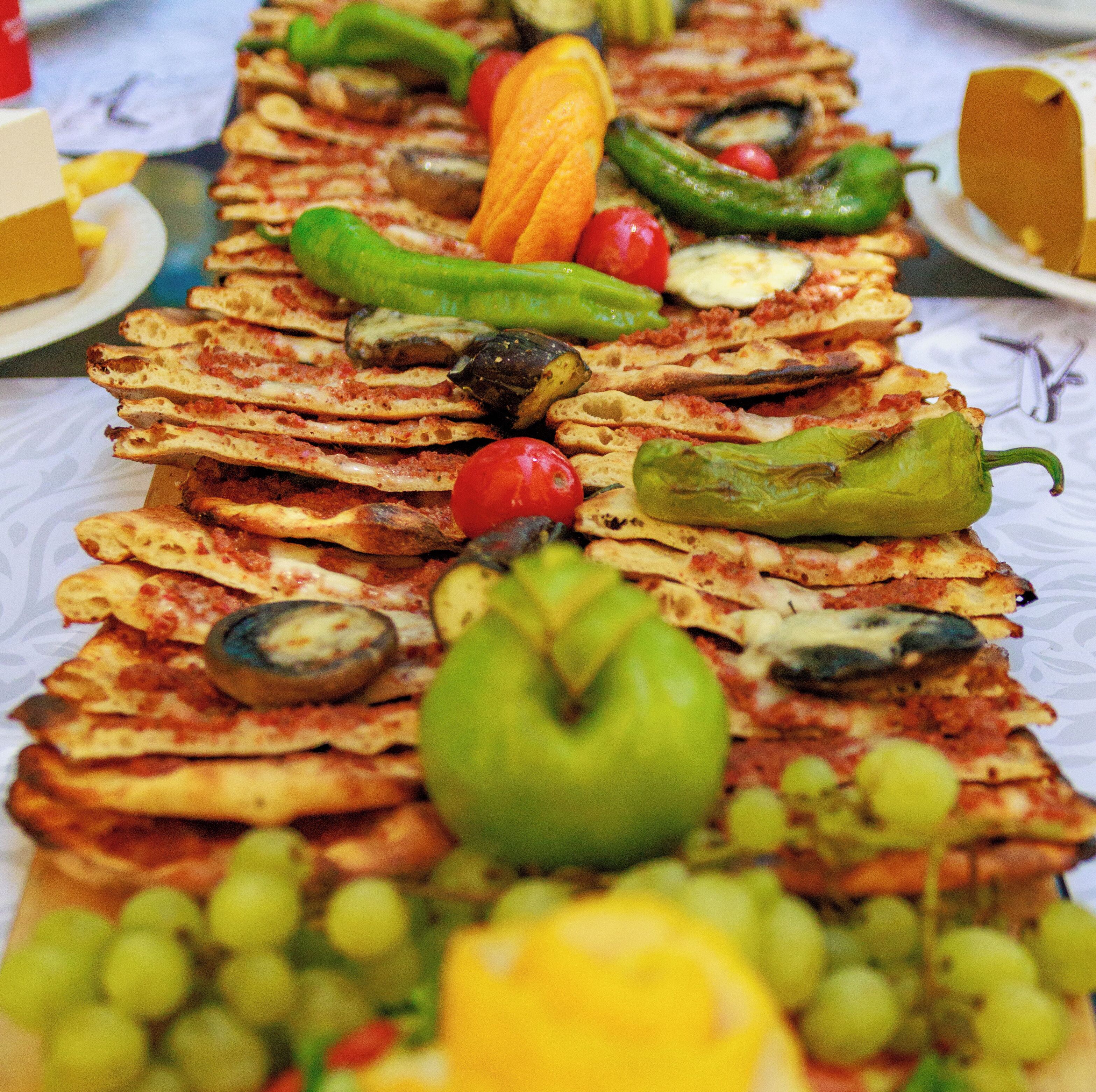 Een tafel met diverse etenswaren, zoals sneetjes brood, tomaten, groene paprika's en druiven.