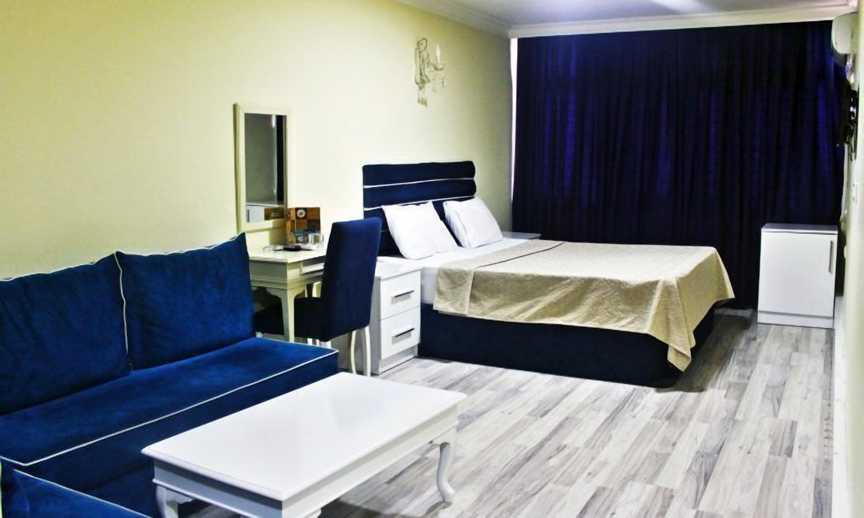 A hotel room with a bed, a sofa, a desk, and a small refrigerator.
